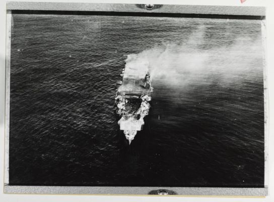 IJN Carrier Hiryu shown in the center of the image with a massive hole in its forward deck and smoke coming from it.