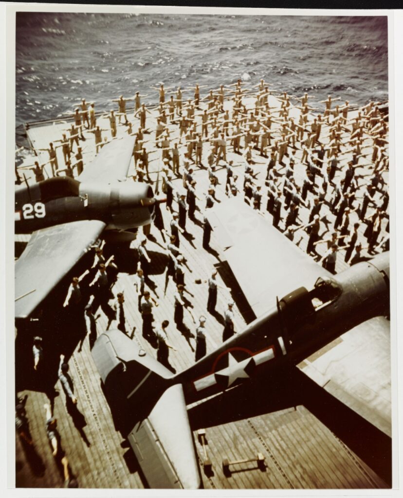 Daily Calisthenics on the flight deck of USS Yorktown CV-10, an Essex class carrier, during the summer of 1943. Planes are Grumman F6F-3 HELLCAT fighters.