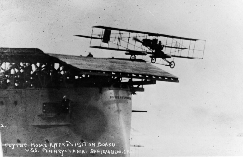 Flying off aircraft platform on USS Pennsylvania (Armored Cruiser # 4), 18 January 1911. Earlier in the day Ely had landed on the ship's deck, the first time an airplane alighted on a warship's deck. Pennsylvania was then anchored in San Francisco Bay, California. Photograph from the Eugene B. Ely scrapbooks. U.S. Naval History and Heritage Command Photograph. NH 77565