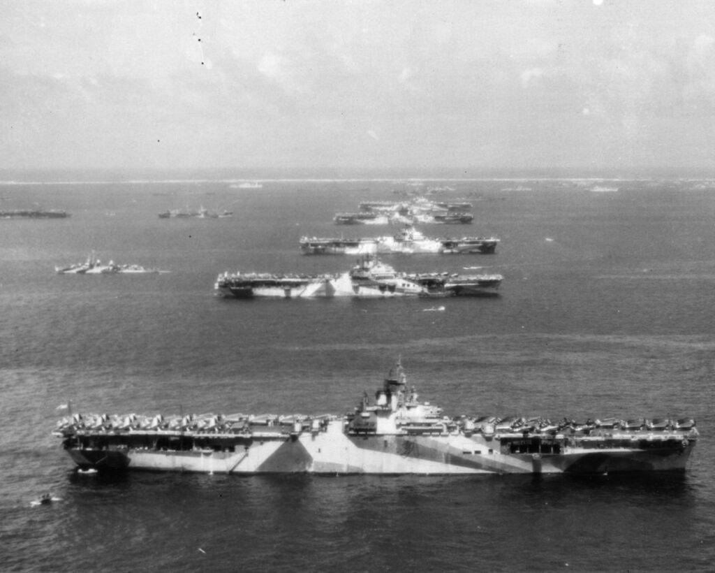 Arial photo of a line of US Essex-class carrriers moored parallel to each other in Ulithi Atoll. USS Wasp (CV-18), USS Yorktown (CV-10), USS Hornet (CV-12), USS Hancock (CV-19) and USS Ticonderoga (CV-14). Official U.S. Navy Photograph 80-G-294131