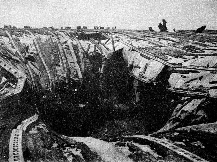 A massive hole with bent metal girders and broken wooden boards is shown in the USS Franklin's flight deck. US Navy Photo.