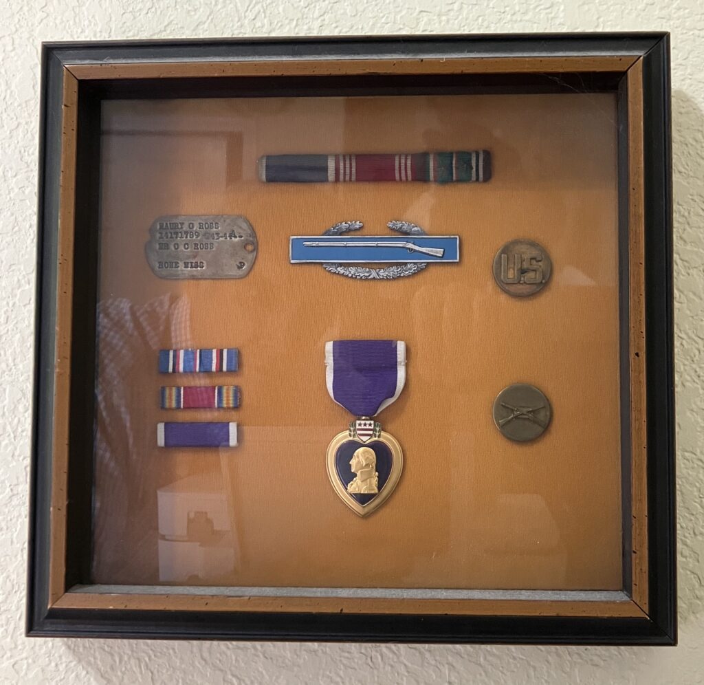 Shadow box conaining the Purple Heart, dog tag, Infantryman's combat badge and other ribbons from Sergeant Maury Ross. He saw combat while serving in the 102nd "Ozark" Infantry division in WWII.