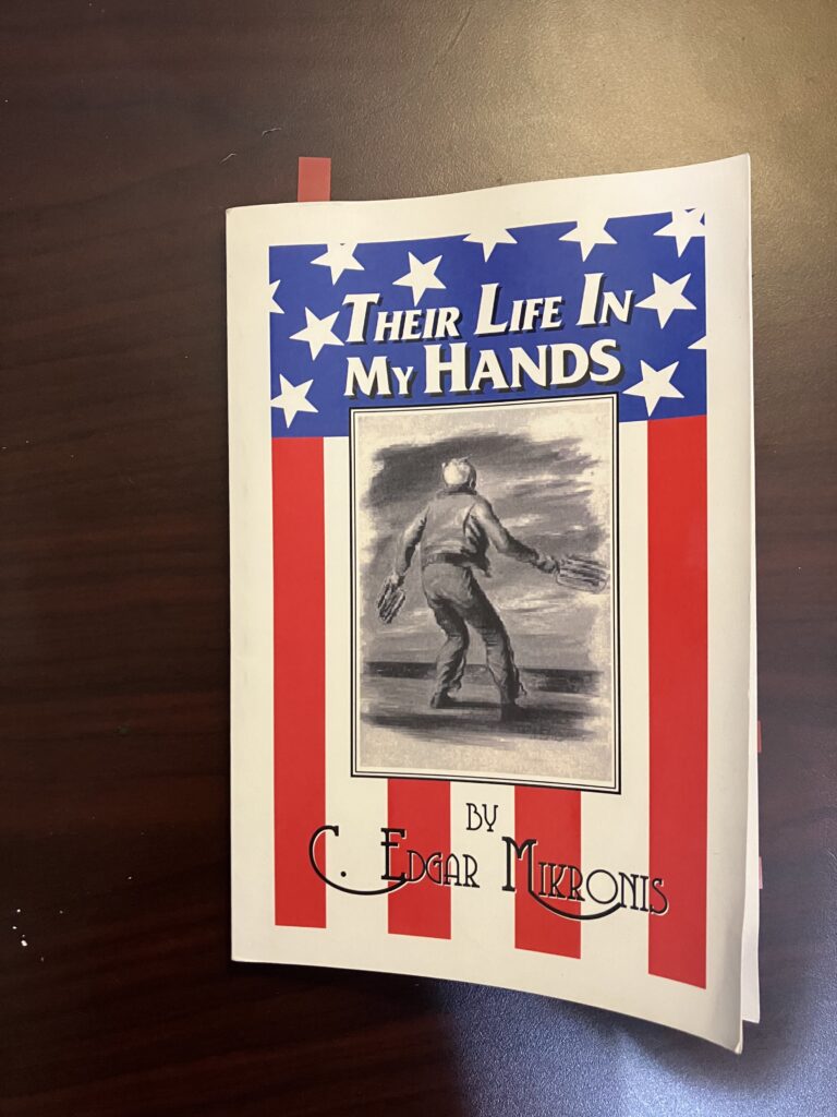 Cover of the book, "Their Life In My Hands." Centered is a pencil sketch of a US Navy Landing Signal Officer with paddles in his hands. The view is from the back. This is a photo by the author of this blog post.