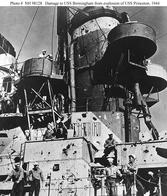 Looking up from USS Birmingham's forecastle, it shows a dozen or so of the crew standin around amid damage caused to the superstructure and funnel by the USS Princeton's explosion while the cruiser was 50 feet away.