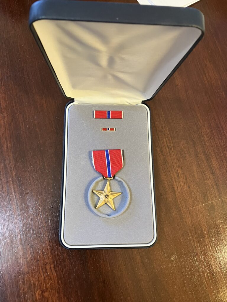 Image of a US Military award, The Bronze Star, in its presentation box sitting on a desk. Awarded to Maury Ross for action against the Germans in 1944.