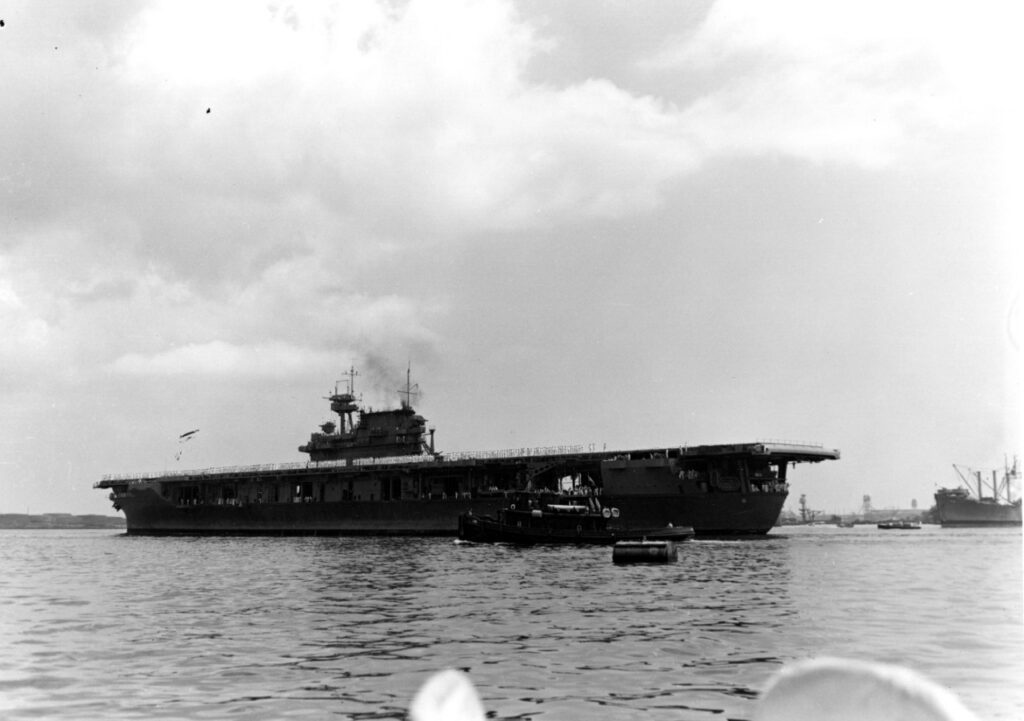 USS Yorktown shown arriving at Pearl Harbor after the Battle of Coral Sea. The picture is taken several hundred yards away and you can see the entire ship with the bow to the right and the stern to the left.