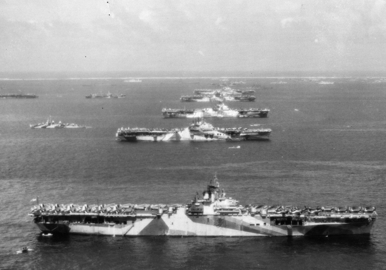 Arial photo of a line of US Essex-class carrriers moored parallel to each other in Ulithi Atoll. USS Wasp (CV-18), USS Yorktown (CV-10), USS Hornet (CV-12), USS Hancock (CV-19) and USS Ticonderoga (CV-14). Official U.S. Navy Photograph 80-G-294131