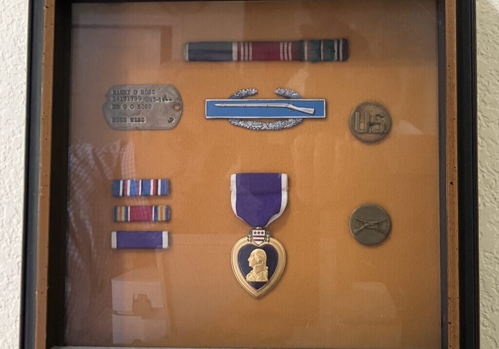 Shadow box conaining the Purple Heart, dog tag, Infantryman's combat badge and other ribbons from Sergeant Maury Ross. He saw combat while serving in the 102nd "Ozark" Infantry division in WWII.