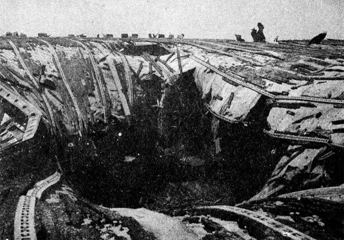 A massive hole with bent metal girders and broken wooden boards is shown in the USS Franklin's flight deck. US Navy Photo.