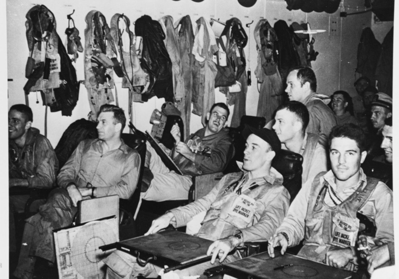 11 Pilots of Torpedo Squadron 13 (VT-13) in their ready room aboard USS Franklin (CV-13), 24 October 1944, just before the Battle of the Sibuyan Sea. They are watching as the position of the Japanese fleet is posted. VT-13's Commanding Officer, Lieutenant Commander Larry French, is second from the left, with a navigation board beside his chair. Note life vests, with die marker pouches, worn by several of these men. Other life vests, and .38 caliber revolvers, are hanging on the bulkhead. Official U.S. Navy Photograph, 80-G-290733