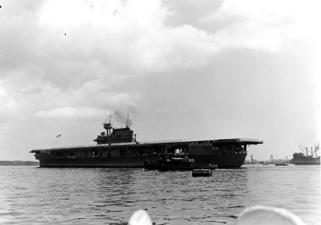 USS Yorktown shown arriving at Pearl Harbor after the Battle of Coral Sea. The picture is taken several hundred yards away and you can see the entire ship with the bow to the right and the stern to the left.